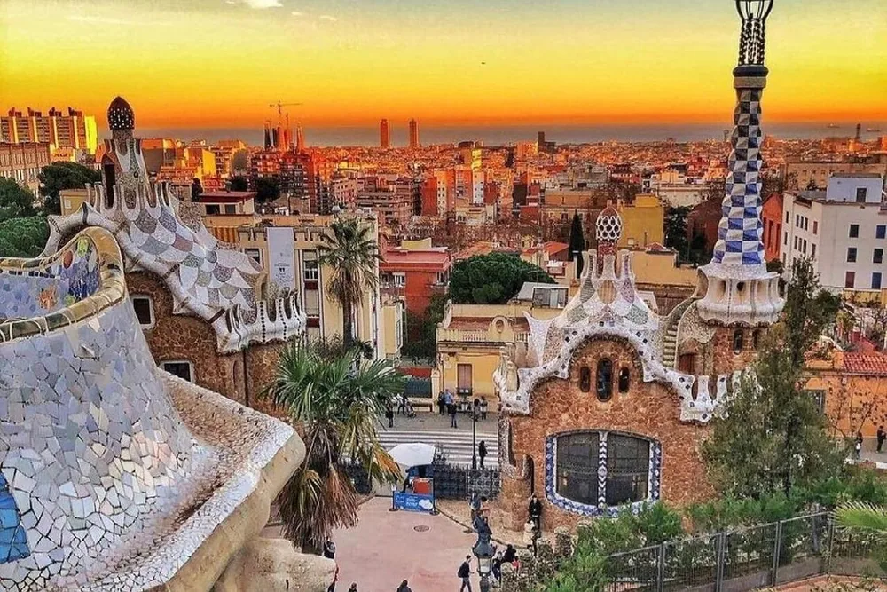 Las casetas de mosaico de Park Güell al atardecer con la ciudad de fondo